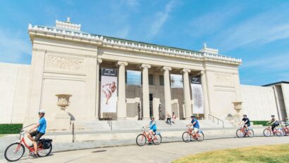 A group rides their bikes in front of a mausoleum in New Orleans, Louisiana