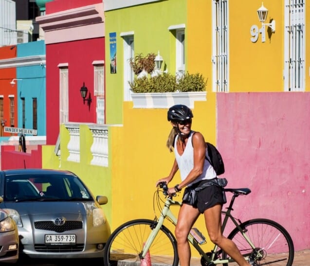 a woman rides her bike in front of the colorful houses of Bo Kapp in Capetown, South Africa