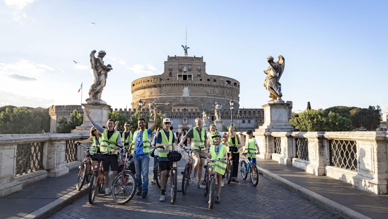 A group of cyclists stops for a photo on a bridge in front of Castel sant'Angelo
