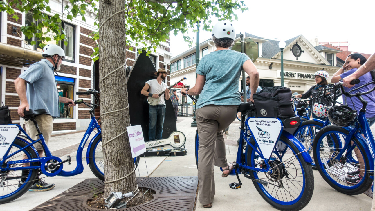 A group of cyclists enjoy a city busker in Asheville, North Carolina