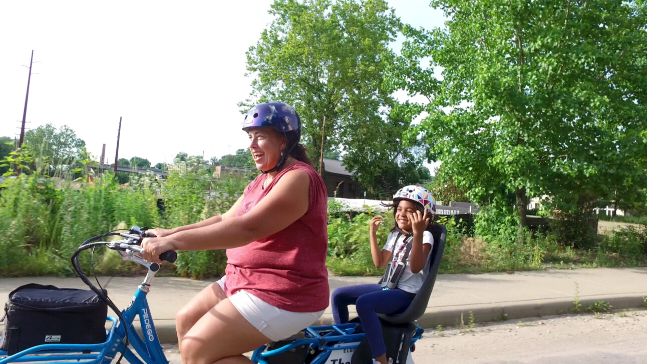 A mom and daughter ride a cargo bike while wearing helmets