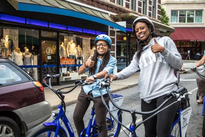 Two female cyclists smile and give a thumbs up to the camera while on a bike tour in Asheville, North Carolina