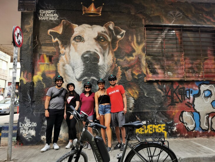 A group of cyclists pose for a photo in front of street art in Athens, Greece