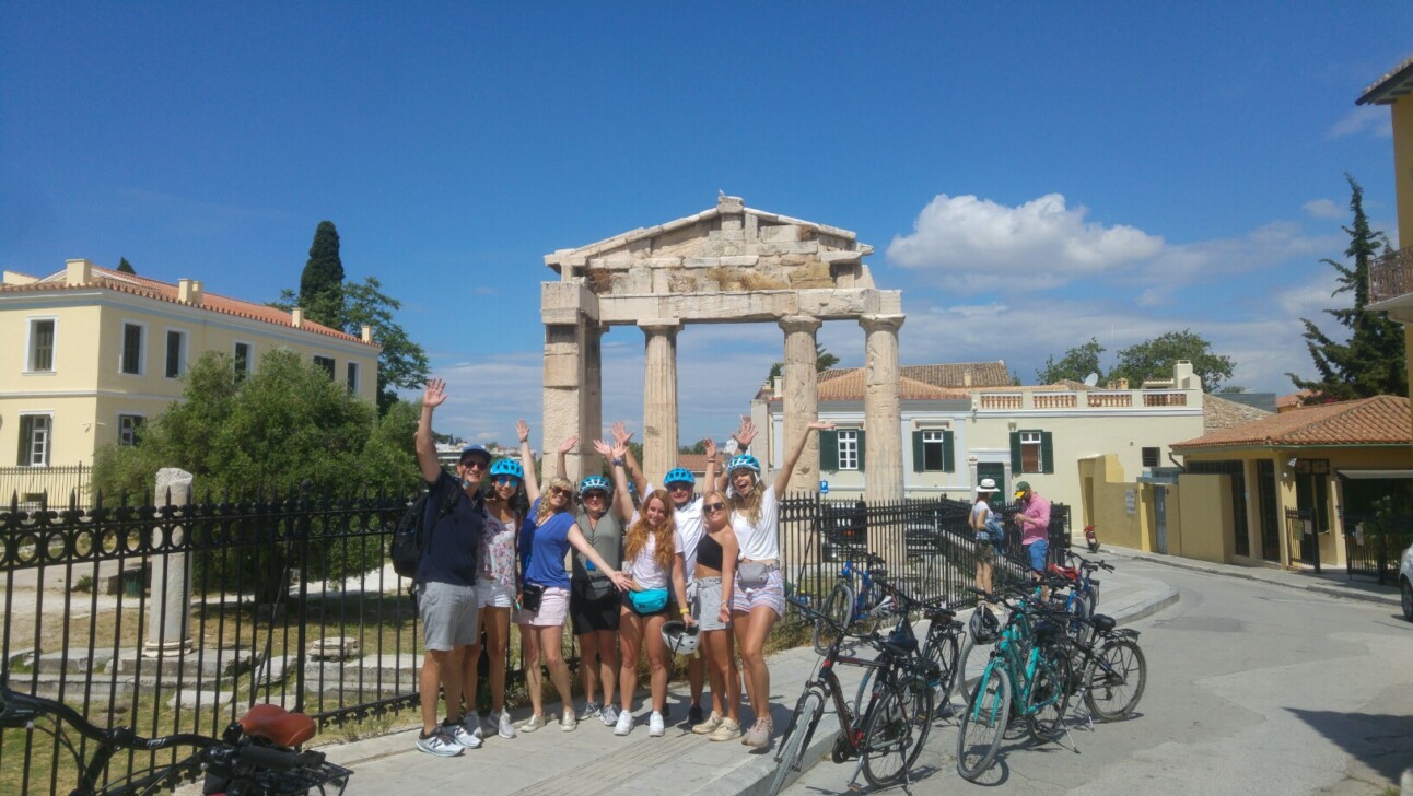 A group of cyclists pose for a photo in front of the Gate of Athena Archegetis in Athens, Greece