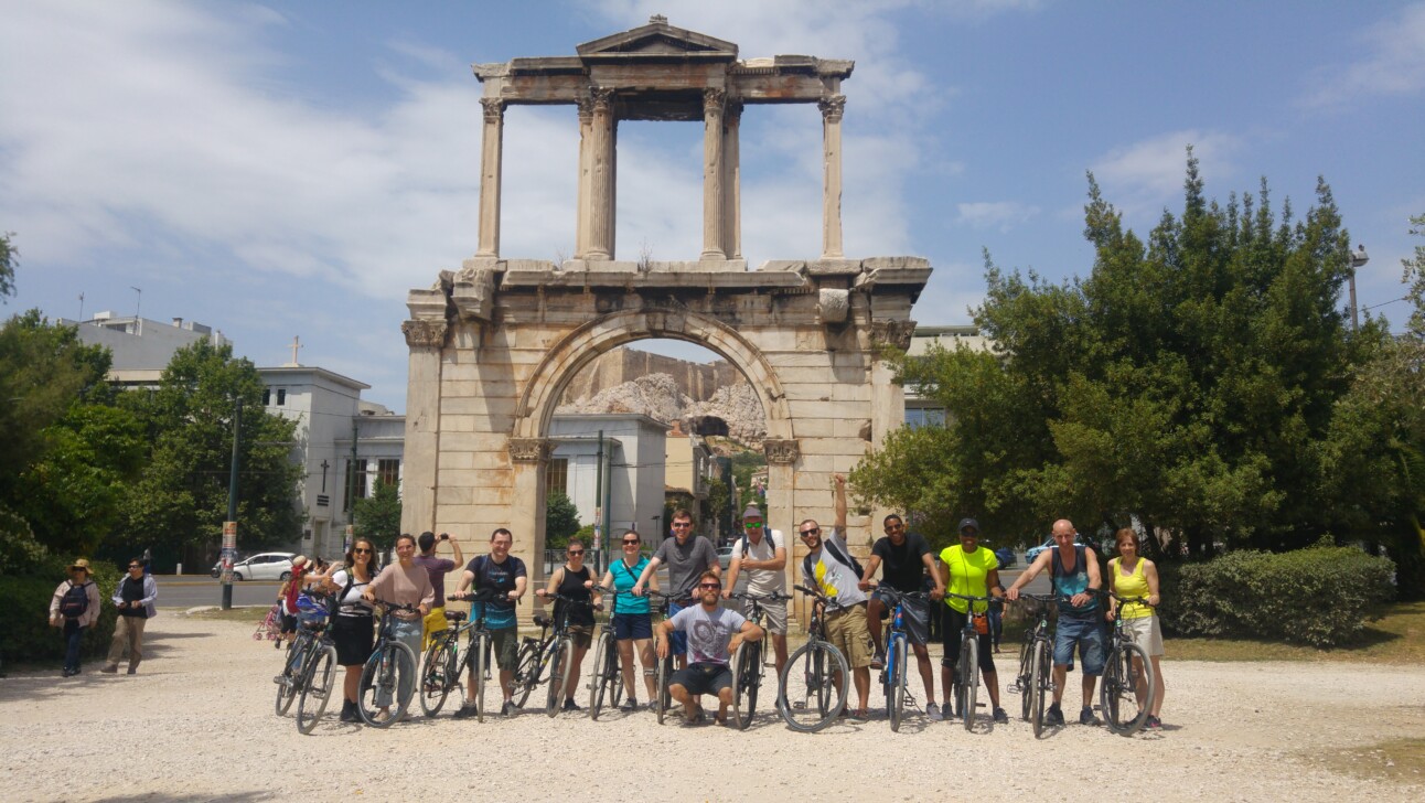 A group of cyclists pose for a photo in front of Hadrian's Arch in Athens, Greece