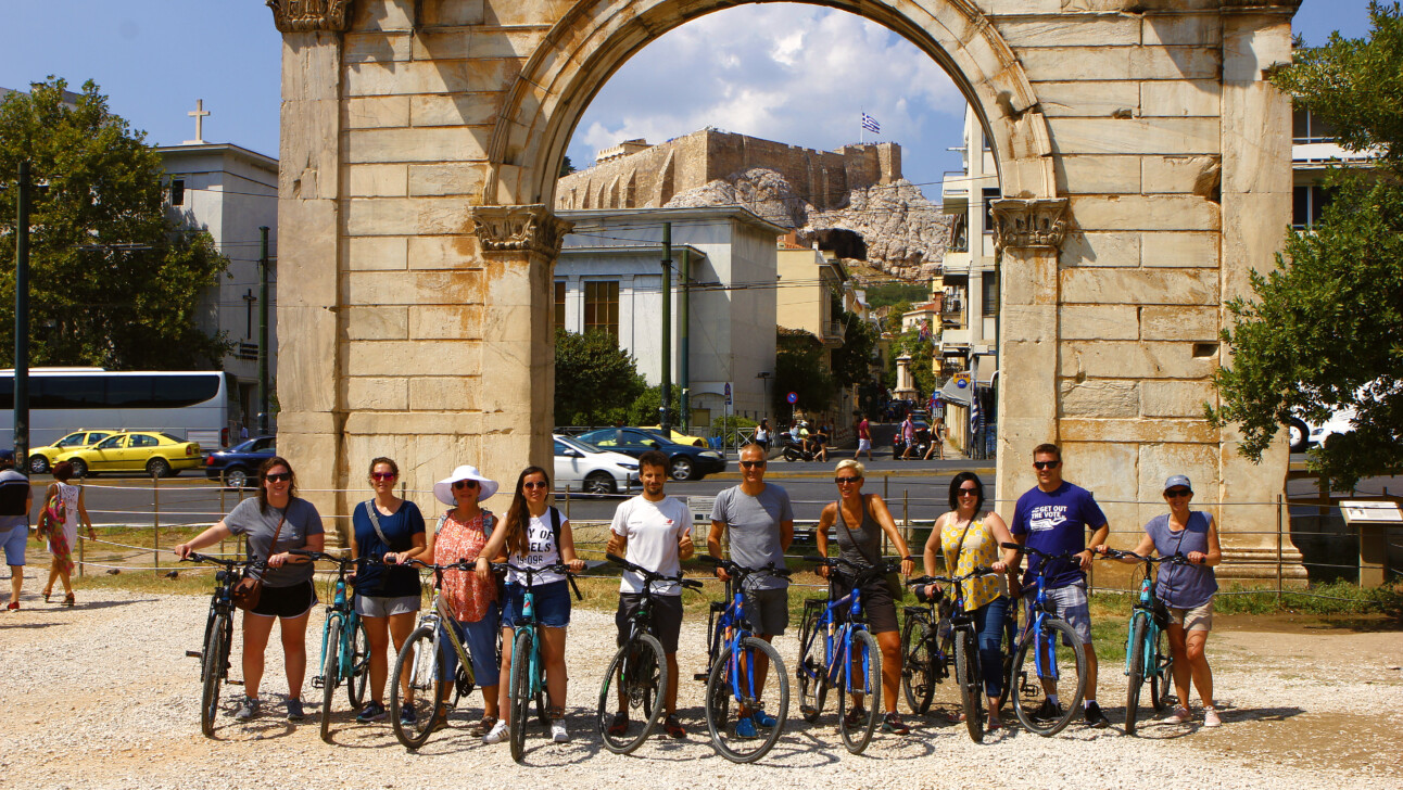 A group of cyclists pose for a photo in front of Hadrian's Arch in Athens, Greece