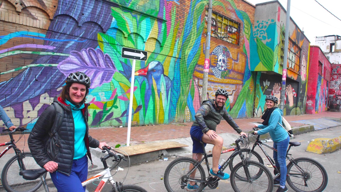 A group of cyclists pose for a photo in front of a street art mural in Bogota, Colombia