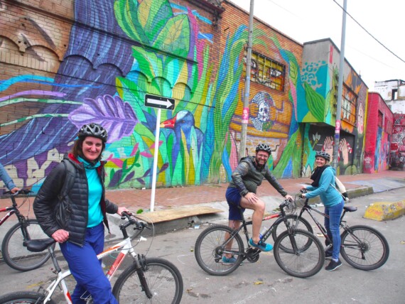 A group of cyclists pose for a photo in front of a street art mural in Bogota, Colombia