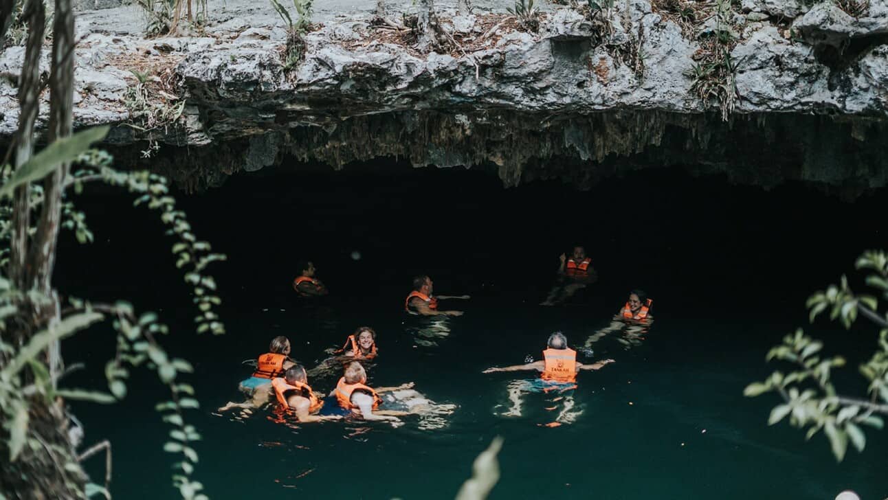 A group swimming in a cenote with orange life jackets on in Tulum, Mexico