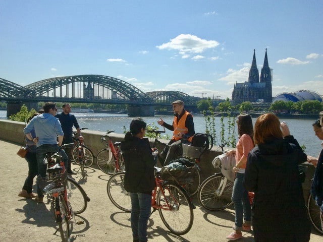 A guide explains the surrounding area to the group with the Hohenzollern Bridge in the background in Cologne, Germany