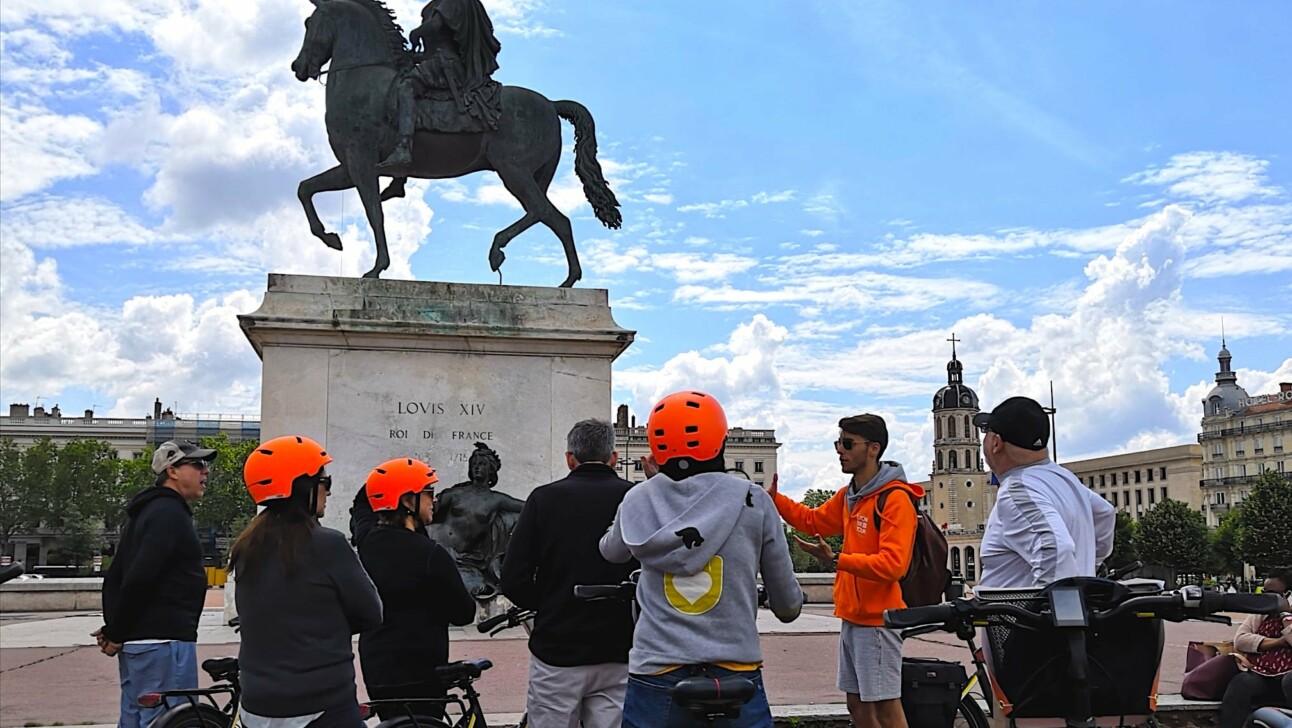A group stands around the Louis XIV statue in Lyon, France as the guide explains the history