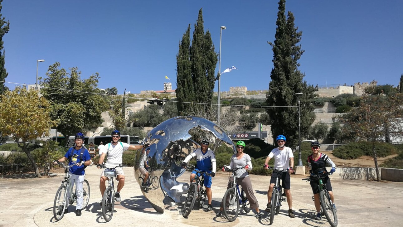 A group of cyclists pose with the 'Jerusalem at the center of the world' sculpture