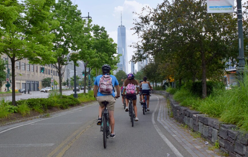 Cyclists ride along a bike path with skyscrapers in the background in New York City
