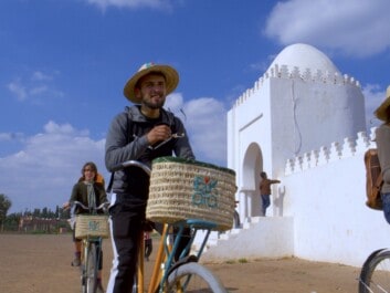 Two people ride in front of a white mosque on bicycles