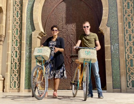 A couple pose with their bikes in front of a mosque