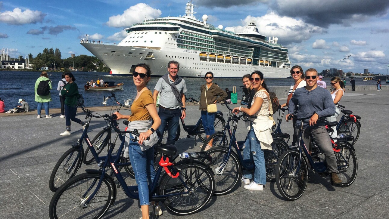 A group of cyclists pose for a photo in Amsterdam in front of a large cruise ship