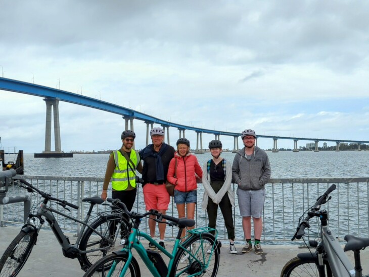 A group of cyclists pose for a photo in front of the Coronado Bridge in San Diego