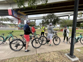 A group of cyclists stop under a graffitied bridge in San Diego
