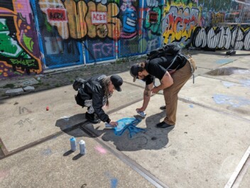 Two people spray painting art onto the sidewalk in Amsterdam