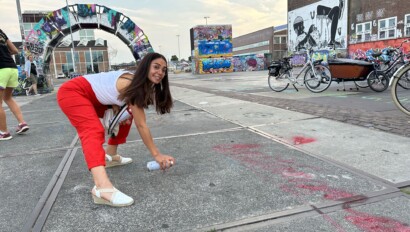 A woman in red pants spray paints onto a sidewalk