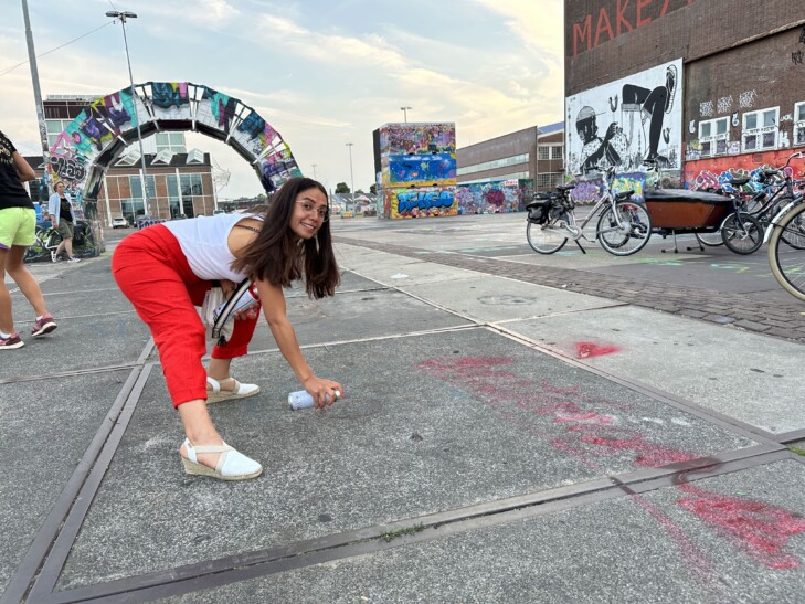 A woman in red pants spray paints onto a sidewalk