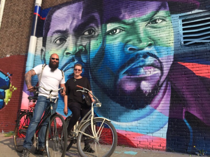 Two cyclists stop for a photo in front of an art mural on a city wall in Amsterdam